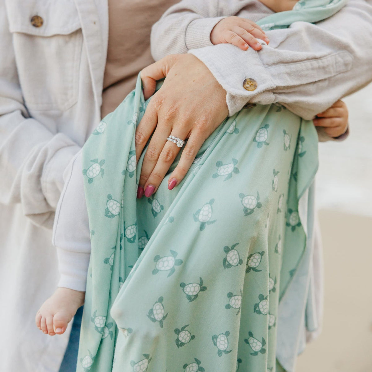 Person holding a child wrapped in a green patterned blanket with a blurred background