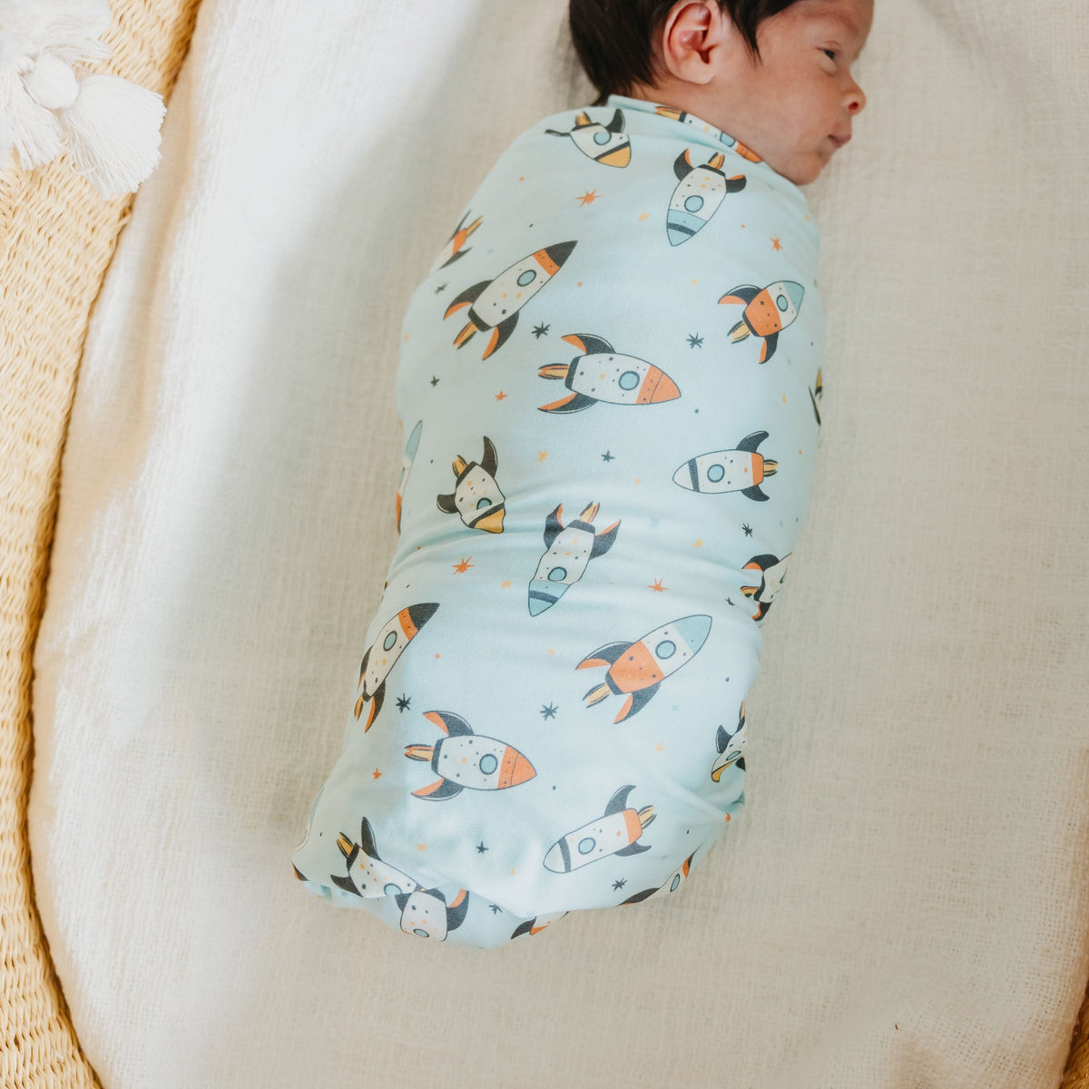 Newborn baby swaddled in a blanket with rocket ship pattern on a beige surface