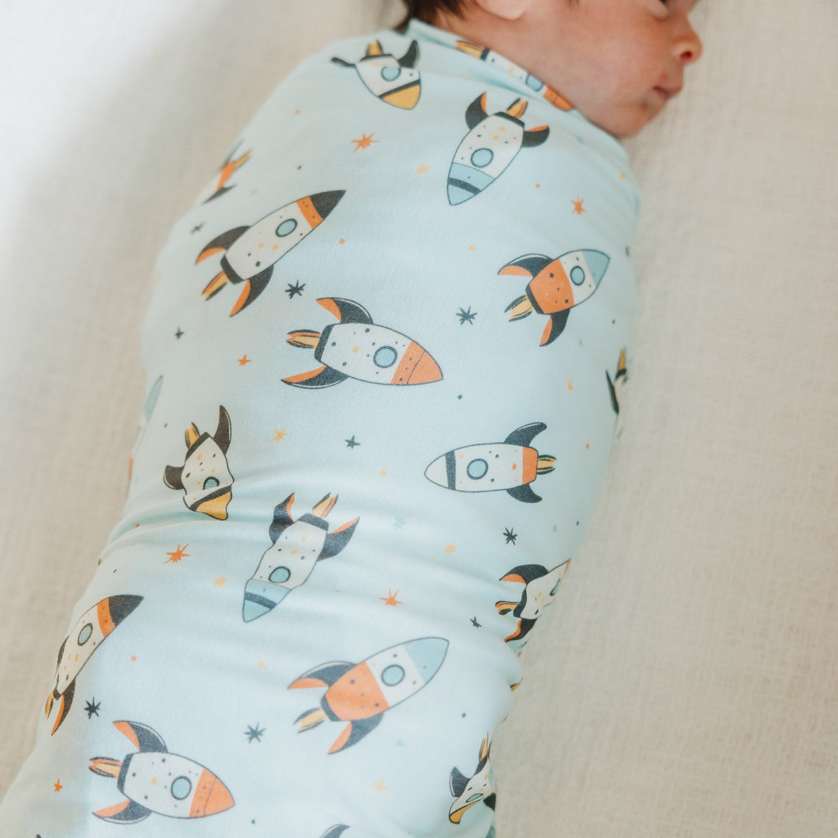 Baby swaddled in a blanket with rocket ship pattern on a neutral background