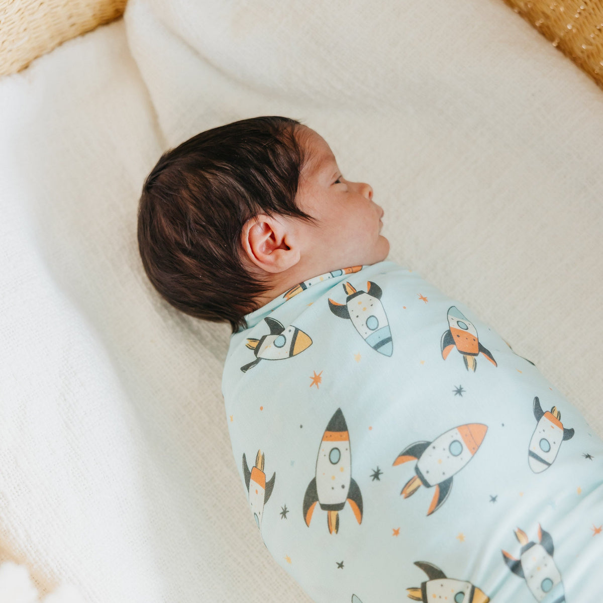 Baby swaddled in a blanket with rocket ship pattern on a soft surface