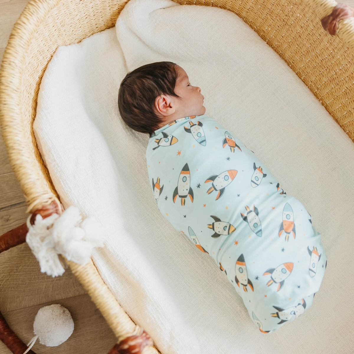 Baby swaddled in a blanket with space-themed design in a wicker crib.