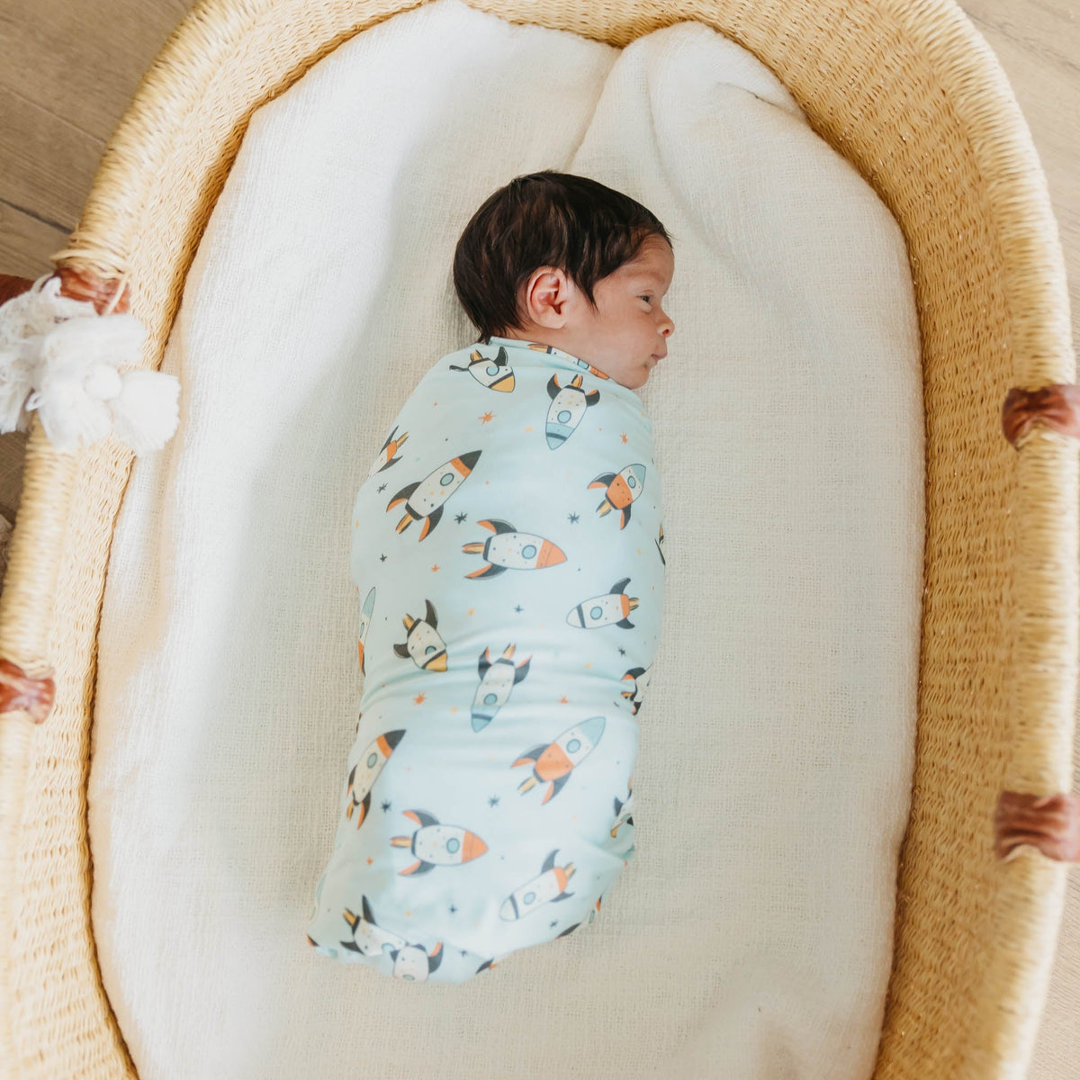 Baby swaddled in a patterned blanket lying in a moses basket.