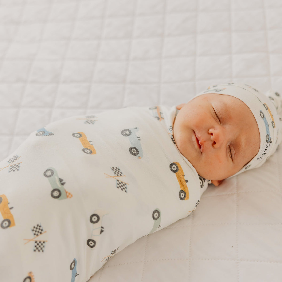 Baby swaddled in a blanket with vehicle patterns on a white background