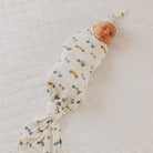 Newborn baby swaddled in a blanket with vehicle pattern on a white quilted surface