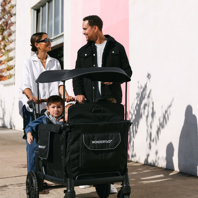 Family with a black WonderFold stroller against a white wall.