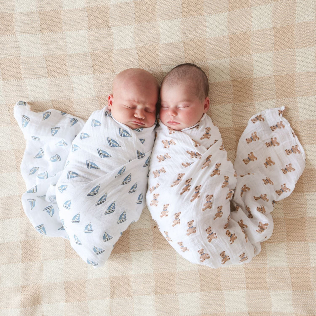 Two swaddled babies lying on a checkered blanket