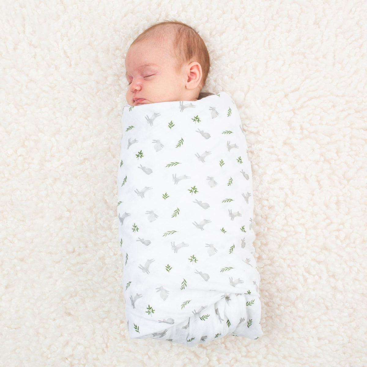 Newborn baby swaddled in a white blanket with green patterns on a soft beige surface