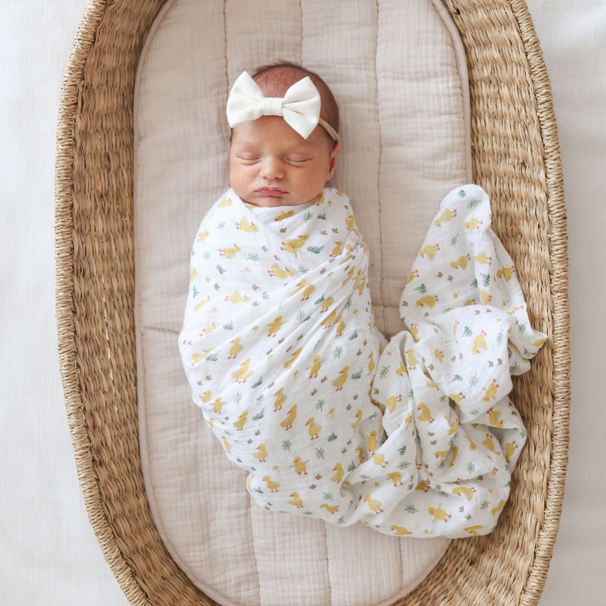 Newborn baby wrapped in a swaddle with a bow, lying in a woven basket.