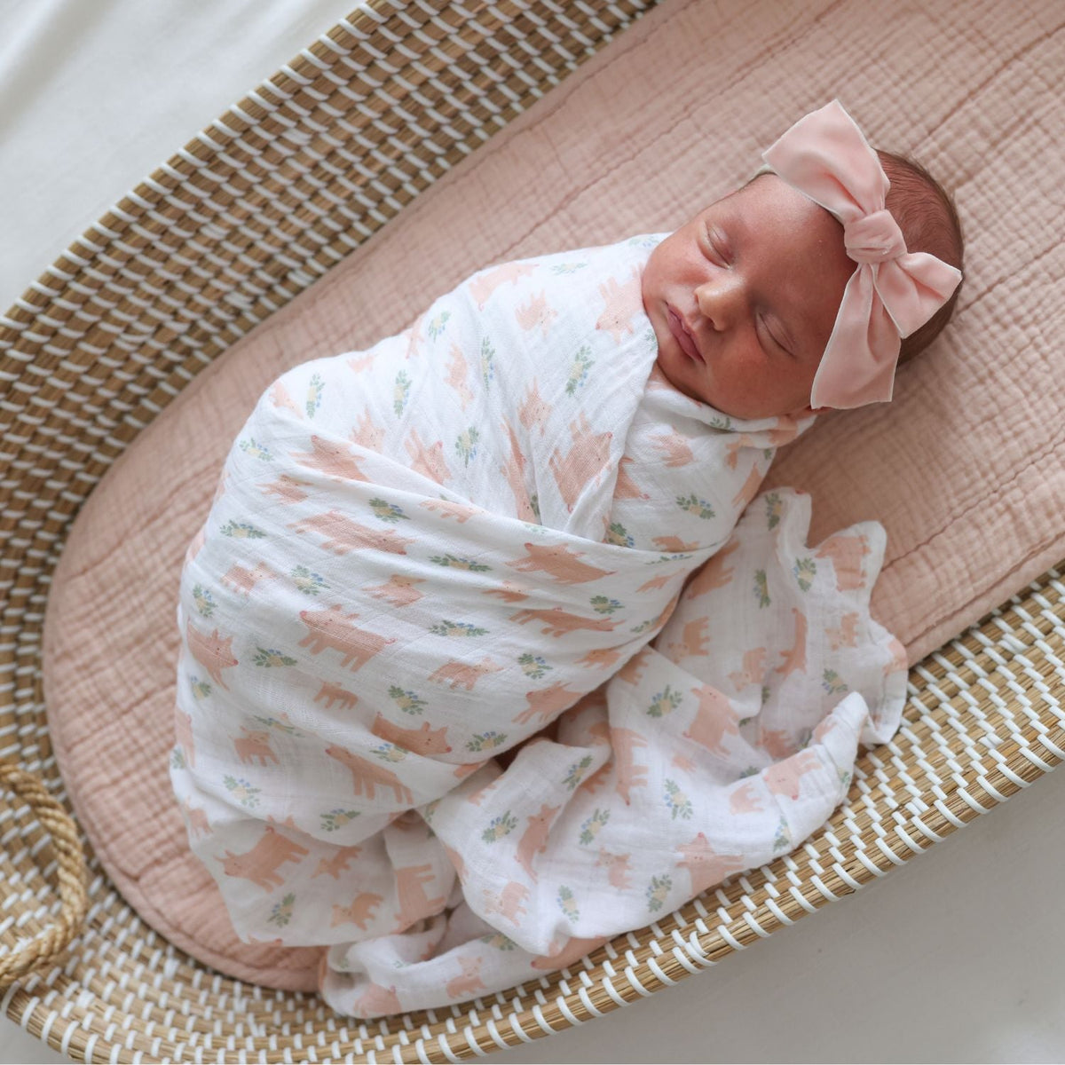 Newborn baby swaddled in a floral blanket with a pink bow on a woven basket.