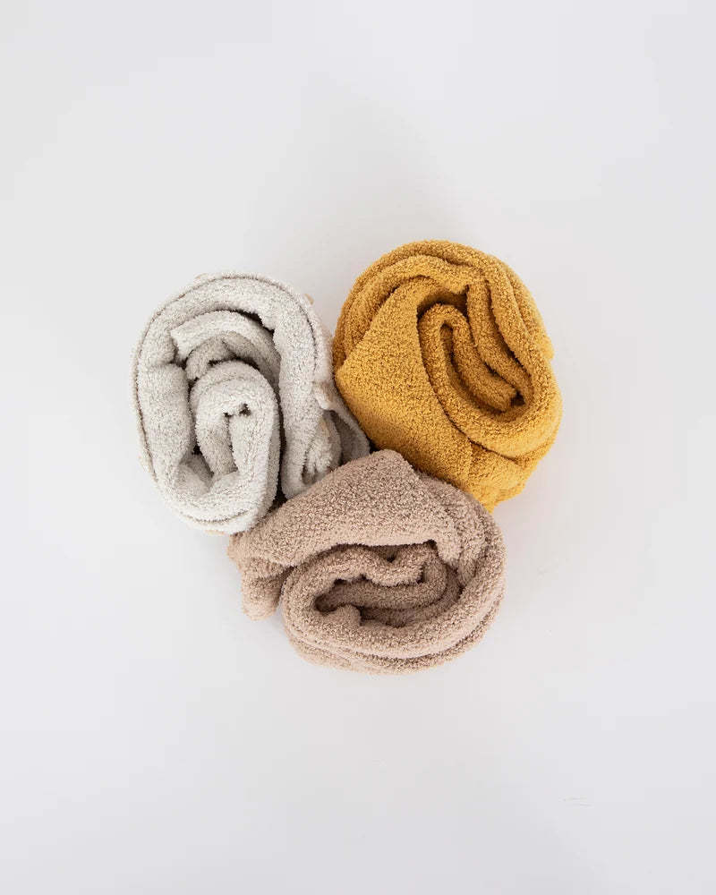 Three rolled-up fuzzy rompers by 7AM Enfant in ecru, mustard yellow, and taupe arranged together on a white background.