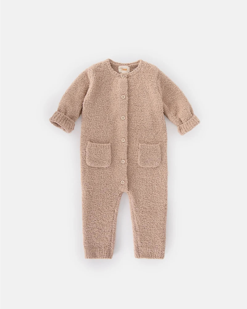 A soft, long-sleeve fuzzy romper in a warm pecan brown color by 7AM Enfant, featuring a round neckline, a full-length center button closure, ribbed cuffs and ankles, and two front pockets, laid flat on a white background.
