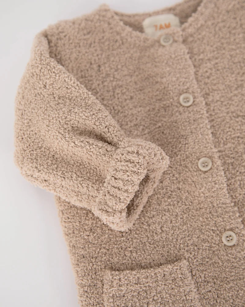 A close-up view of the upper portion of a soft, fuzzy pecan brown romper by 7AM Enfant, highlighting its round neckline, center button placket, folded-up sleeves, and front pocket against a neutral background.