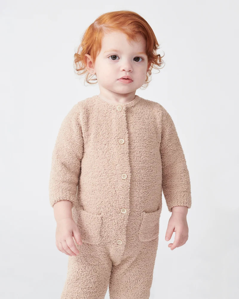 A toddler with reddish-brown hair stands facing forward, wearing a long-sleeve fuzzy romper in a warm pecan brown color by 7AM Enfant, against a plain white background.