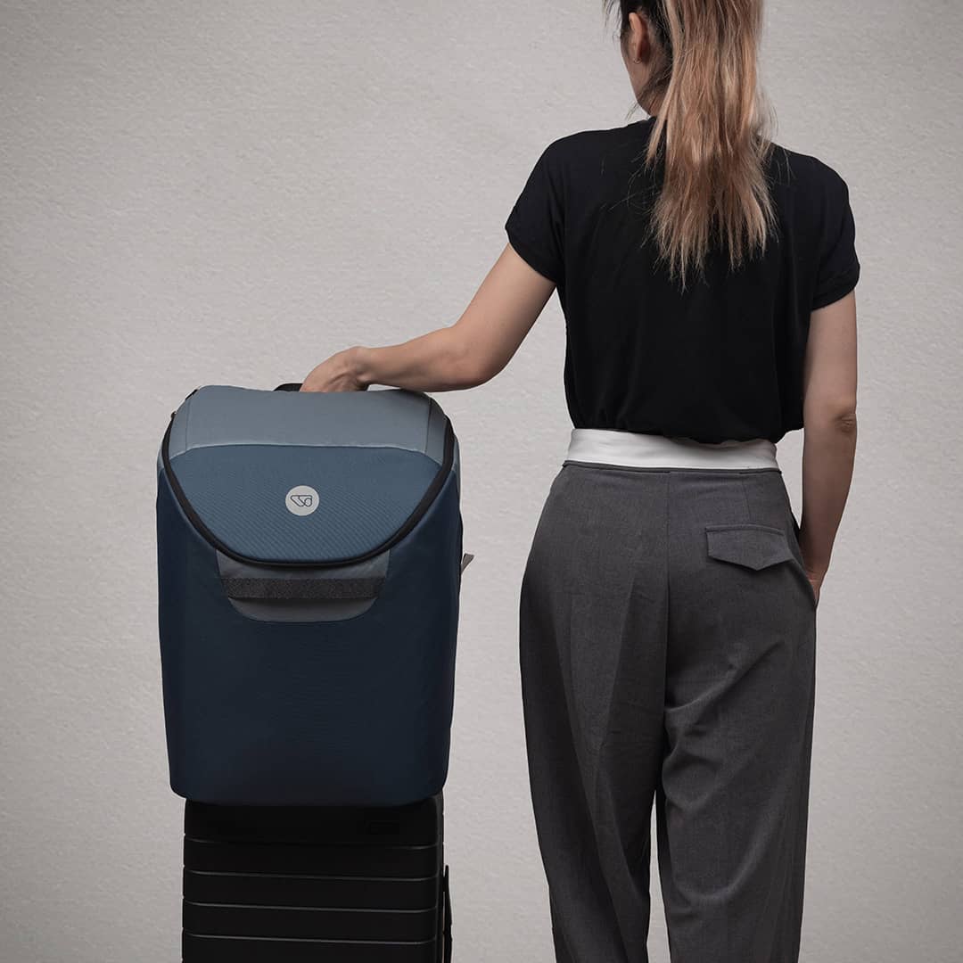Person standing next to a blue suitcase on a gray background