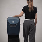 Person standing next to a blue suitcase on a gray background