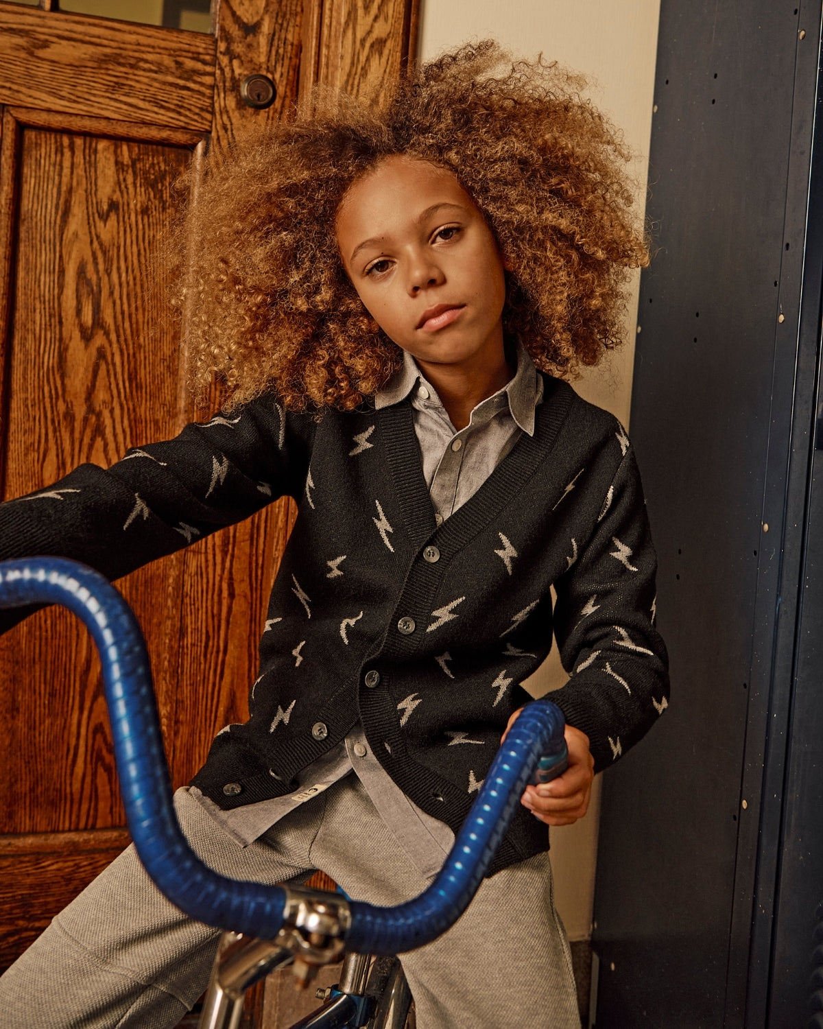 Child wearing a patterned cardigan with a bicycle indoors