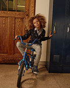 Child with a bicycle in front of a wooden door and blue locker.