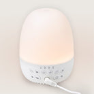 White sound machine with a glowing top on a light beige background