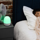 Person sleeping in bed with a night light on a nightstand next to them.
