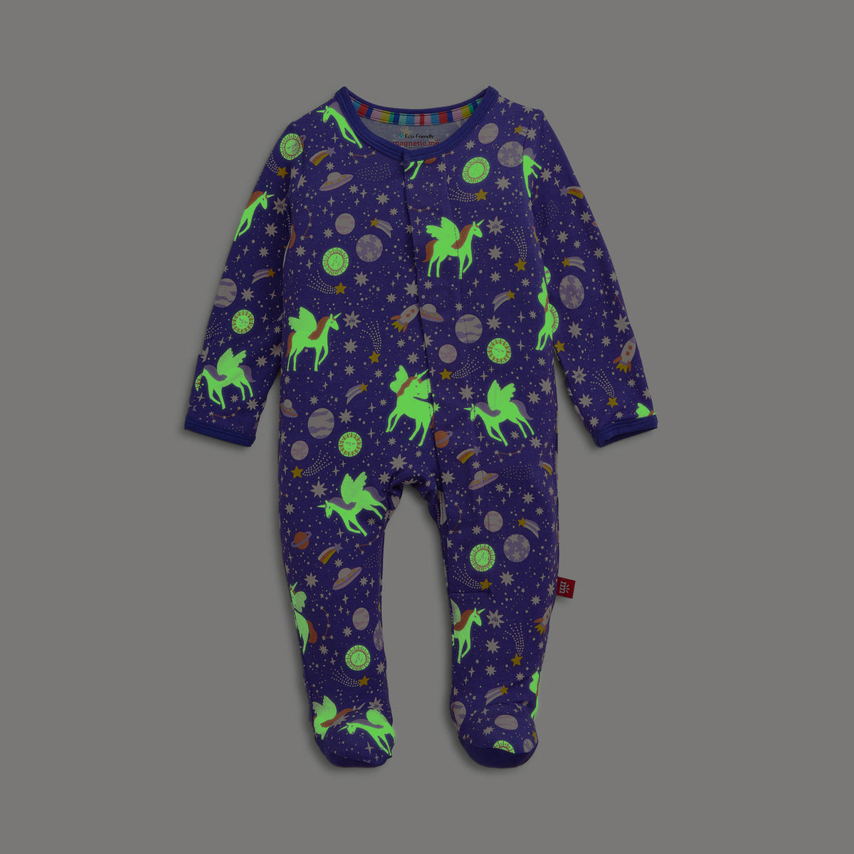 A baby's long-sleeve footed sleeper in a deep purple space theme, featuring neon green glowing unicorns, planets, and stars, displayed flat against a solid gray background.