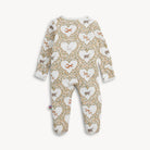 A baby footed one-piece jumpsuit with a long-sleeve design, featuring an all-over pattern of white hearts filled with small dog silhouettes and surrounded by a beige and green floral trellis. The jumpsuit is shown flat against a light off-white background.