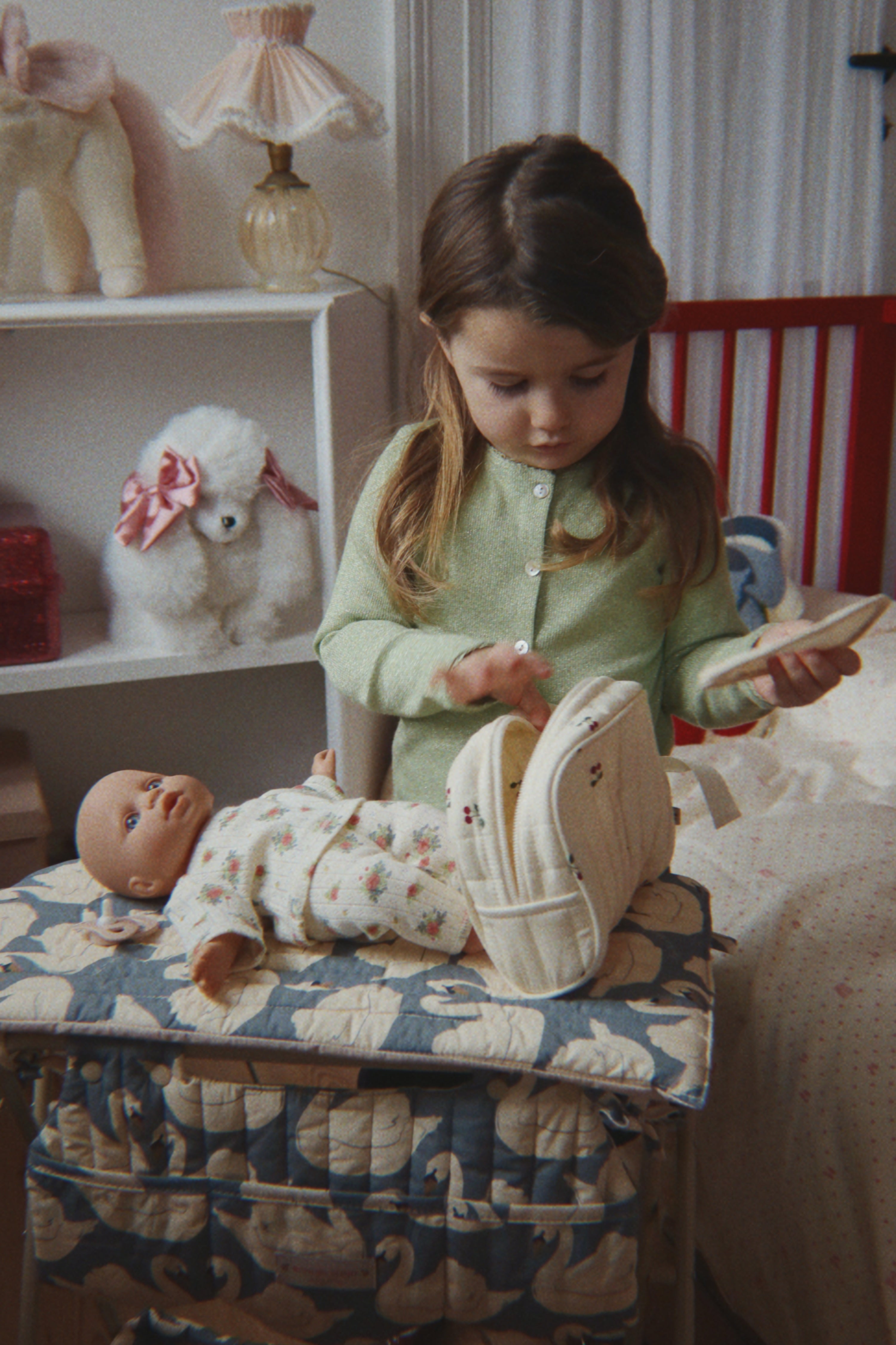Young girl playing with a doll and basket in a bedroom setting.