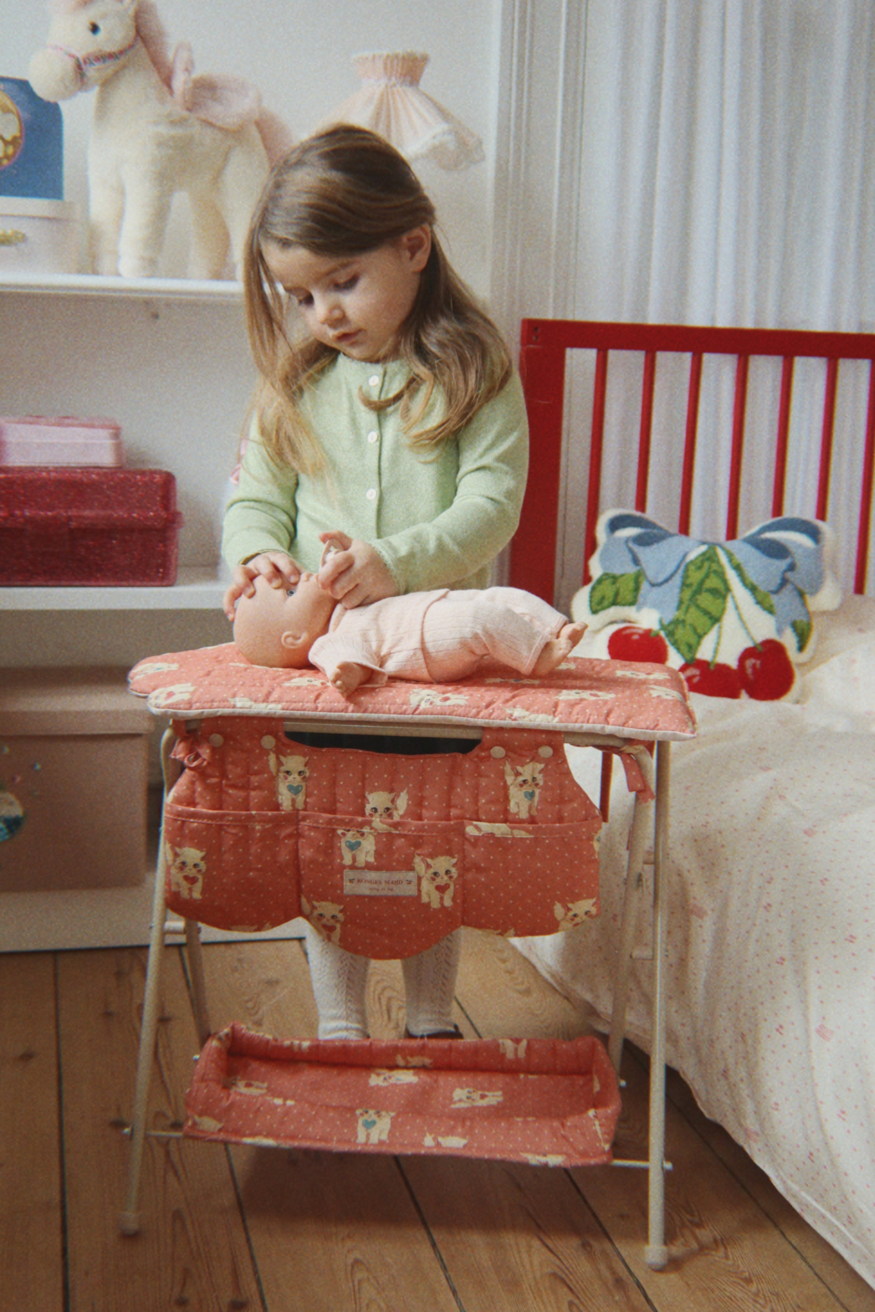 Child playing with a doll on a red and white step stool in a bedroom.