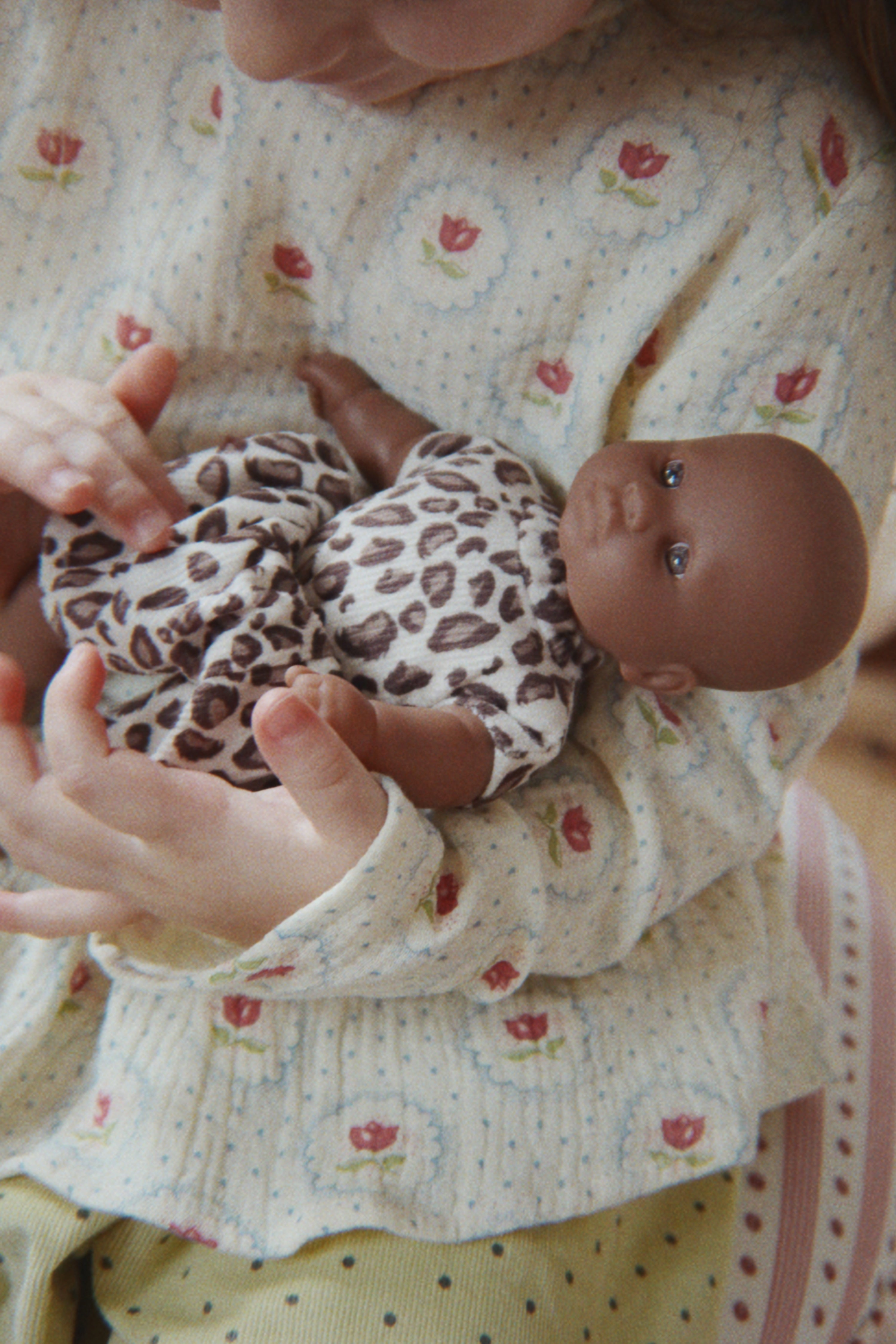 A young girl holding the Konges Sløjd Mini Doll, Leo, a small soft-bodied toy doll dressed in a matching leopard-print outfit.