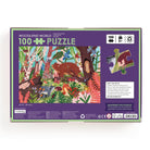 Back of the product box for the Woodland World 100 Piece Puzzle by Mudpuppy, showing the puzzle illustration, artist bio, and a preview of puzzle pieces against a purple background.