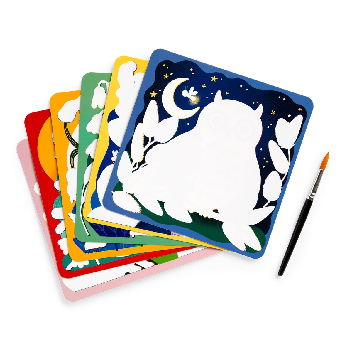 A stack of several colorful, reusable water-reveal boards fan out on a white background, with the top dark blue board featuring a silhouetted white owl and crescent moon design. A paintbrush rests on the right side next to the stack.