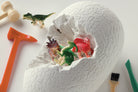A large, cracked white dinosaur egg revealing small toy dinosaurs nestled inside, surrounded by an orange mallet, a small green brush, and other excavation tools on a white background.