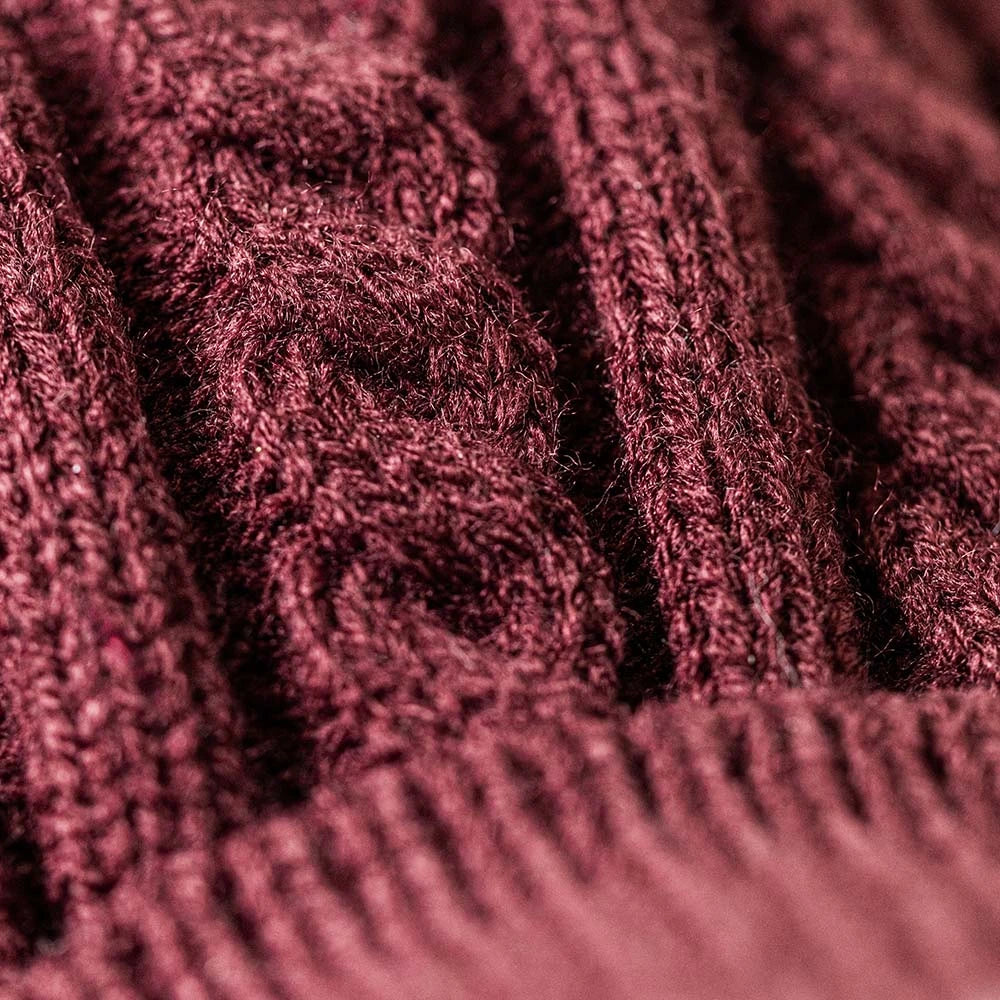 Close-up of a textured knit fabric in a deep burgundy or maroon shade, showing the detailed cable and rib patterns.