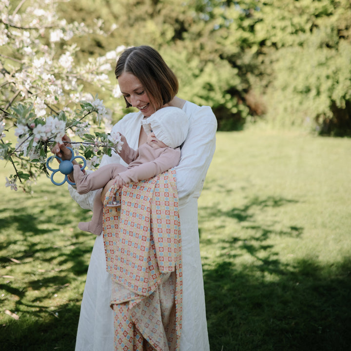 Woman holding a baby in a garden with flowers and greenery