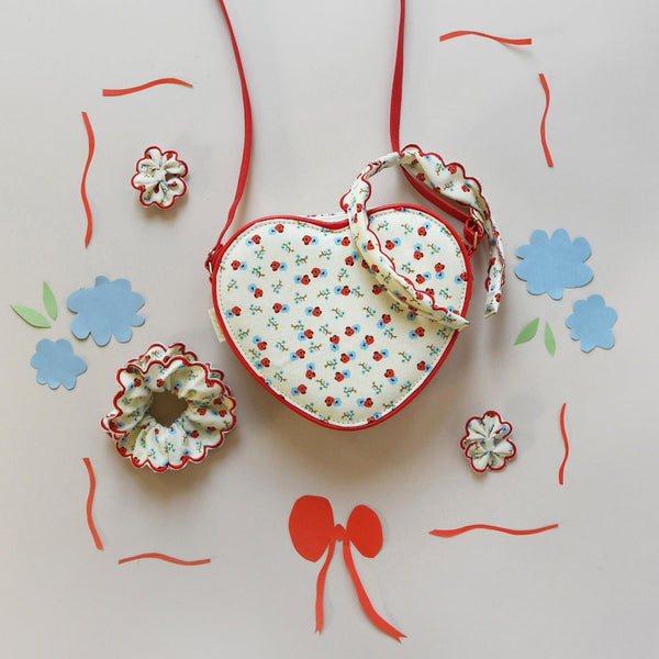 Heart-shaped fabric pouch with floral pattern on a light background with decorative elements.