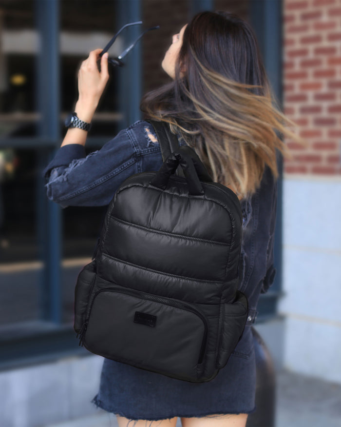 Woman wearing a black backpack outdoors near a building with a brick wall.