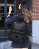 Woman wearing a black backpack outdoors near a building with a brick wall.