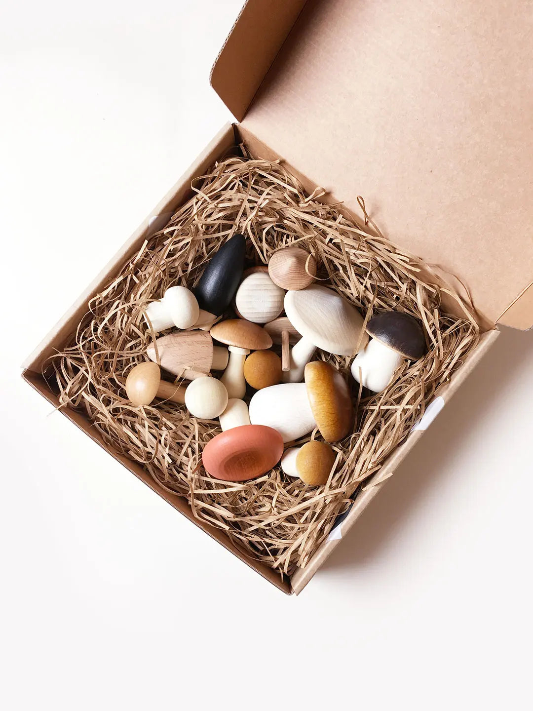 Wooden Mushroom Play Set. The set features assorted mushroom-shaped pieces in natural wood tones and playful colors, presented in a kraft gift-style box with shredded paper filler on a white background.