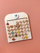 Wooden calendar with decorative numbers and symbols on a pink background