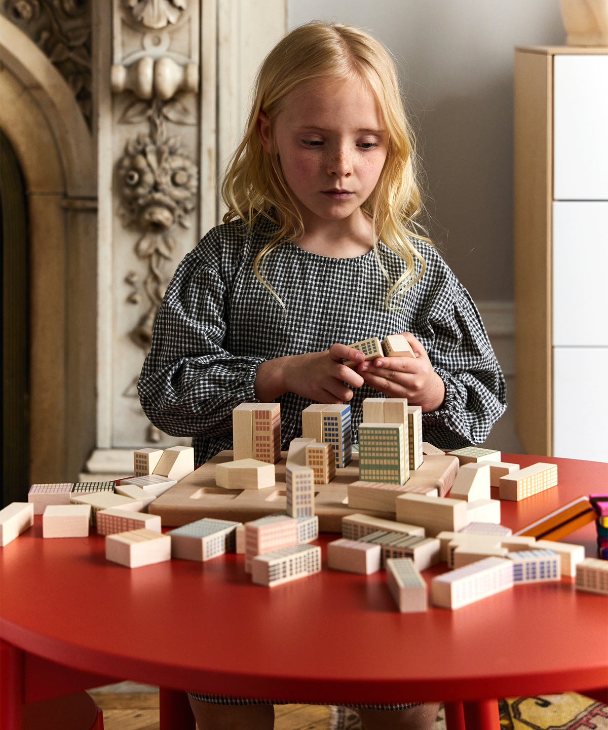 Young girl playing with wooden building blocks on a red table