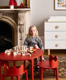 Child playing with building blocks at a red table in a room with a fireplace and white dresser.