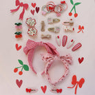 Collection of pink hair accessories including headbands, clips, and bows on a light pink background with decorative elements.
