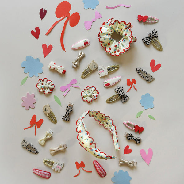 A flat-lay collection of various fabric hair clips and hair accessories arranged on a light gray background, featuring floral patterns, leopard print, bows, and ribbon details.