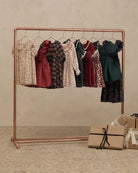 A copper-colored clothing rack holding multiple vintage-style dresses in assorted patterns and colors, set against a textured beige wall with wrapped gift boxes on the floor.
