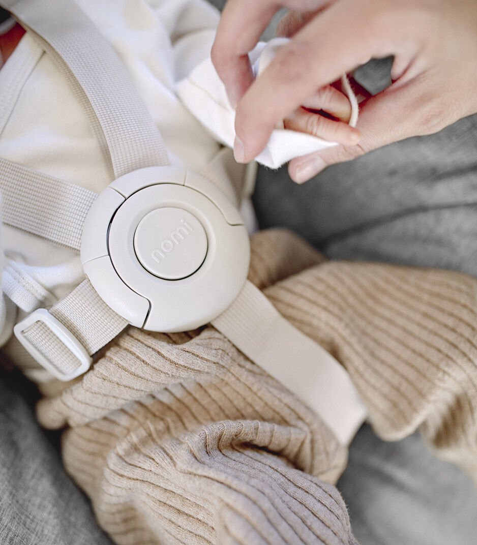 Close-up of a baby seat with a hand cleaning it using a cloth.