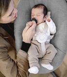 Newborn baby in a gray bouncer with a woman holding the baby's hand.