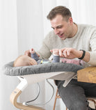 Man sitting with a baby in a modern baby seat against a white curtain background