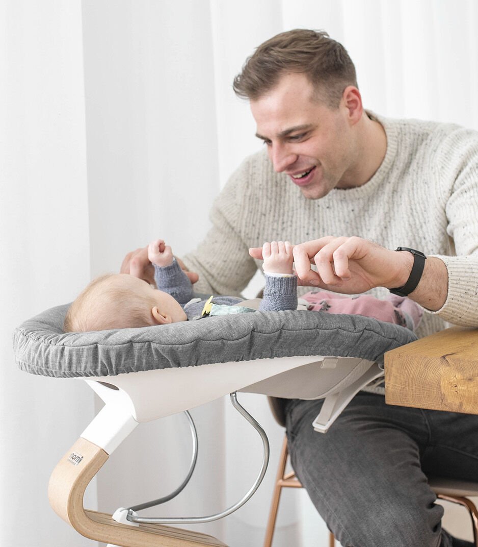Man sitting with a baby in a modern baby seat against a white curtain background