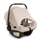 A profile view of a MIXX Next + Pipa Aire RX Travel System by Nuna infant car seat in Biscotti featuring a beige seat and canopy, a brown leatherette carry handle, and safety harness straps with magnetic buckle holders, set against a clean white background.