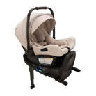 A profile view of a MIXX Next + Pipa Aire RX Travel System by Nuna infant car seat in Biscotti attached to its base with a load leg, featuring a beige seat and canopy and a brown leatherette carry handle, set against a clean white background.