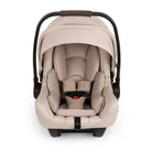 A front view of a MIXX Next + Pipa Aire RX Travel System by Nuna infant car seat in Biscotti featuring a beige seat with matching head and body inserts, a brown leatherette carry handle, and safety harness straps with magnetic buckle holders, set against a clean white background.
